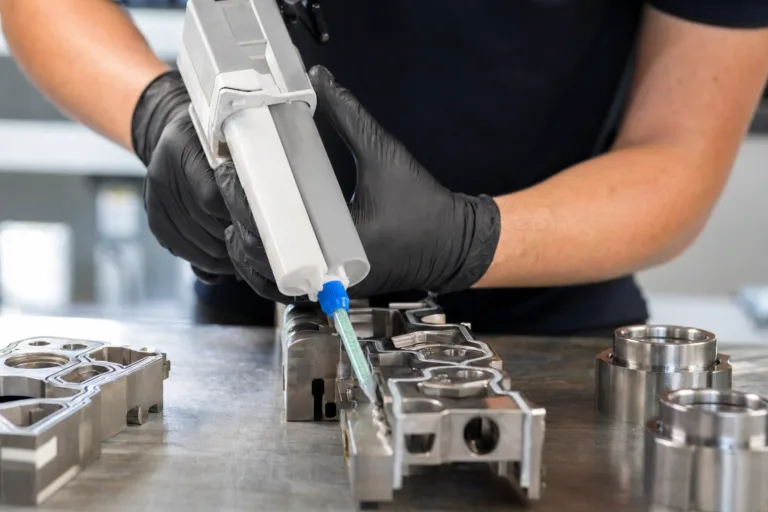 A realistic industrial scene showing two-part structural epoxy being dispensed during precision bonding of metal components.