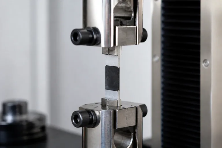 Adhesive Sample & Testing Support 2 A realistic industrial lab scene showing adhesive bond strength evaluation with bonded coupons under mechanical pull testing, captured in a clean professional photographic style.