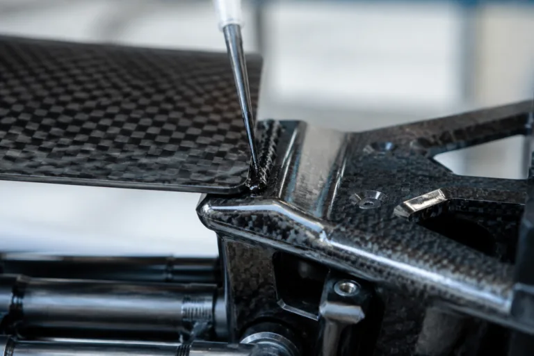 Composite Adhesive 4 A realistic close-up product photo of structural adhesive application on a carbon fiber composite assembly, highlighting the precise bonding area and lightweight advanced equipment details.