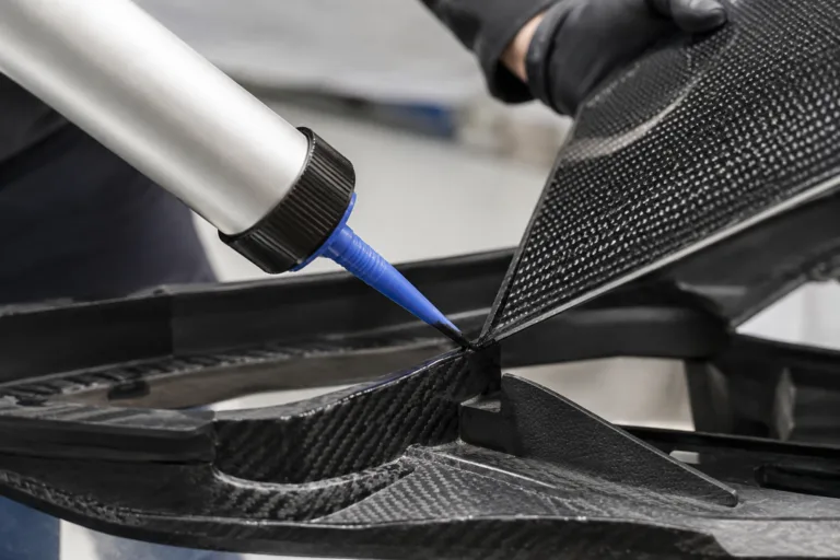 Carbon Fiber Adhesive 7 A realistic close-up industrial product image showing adhesive application during the assembly of a lightweight carbon fiber panel into a supporting frame or shell, with precise craftsmanship and clean manufacturing detail.