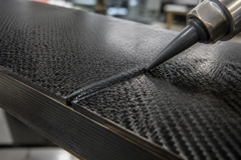 Carbon Fiber Adhesive 5 A realistic close-up industrial scene showing carbon fiber composite components being bonded with structural adhesive in a precise lightweight assembly process.