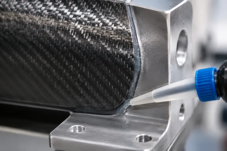 Carbon Fiber Adhesive 4 A realistic close-up product-style image showing adhesive joining a carbon fiber composite panel or tube to an aluminum or stainless steel bracket, emphasizing the hybrid structural bond and precision manufacturing details.