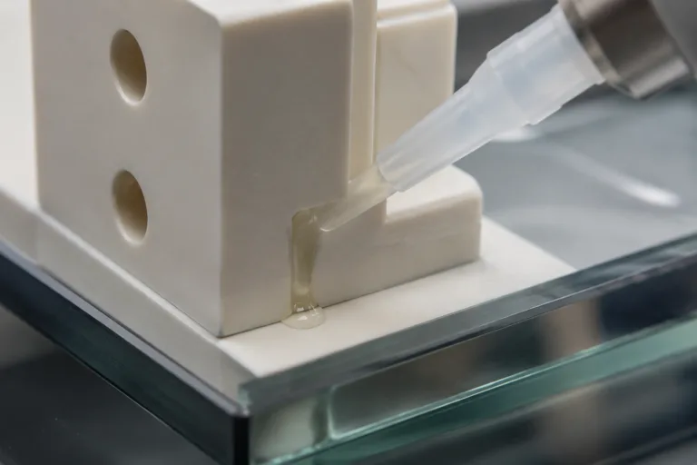 Ceramic Adhesive 4 Professional macro product photography of adhesive bonding a ceramic component to a glass panel, emphasizing the mixed-material joint, precision assembly, and realistic industrial lighting.