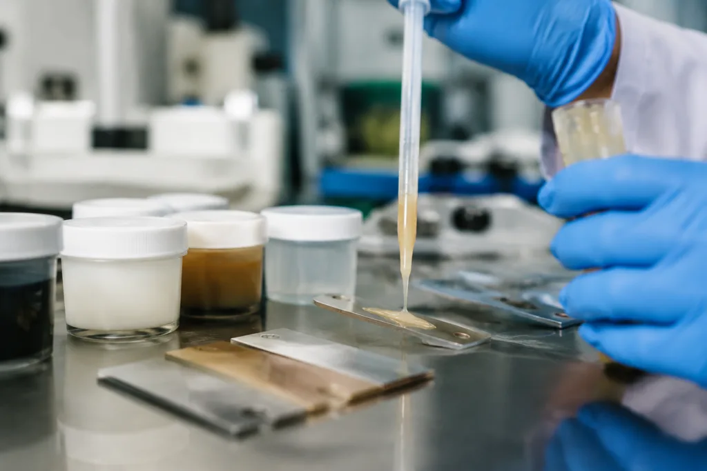 Bonding Adhesive 9 A professional industrial scene showing custom bonding adhesive development and formulation testing, with sample containers, dispensing tools, and bonded material test pieces in a lab-meets-manufacturing setting.