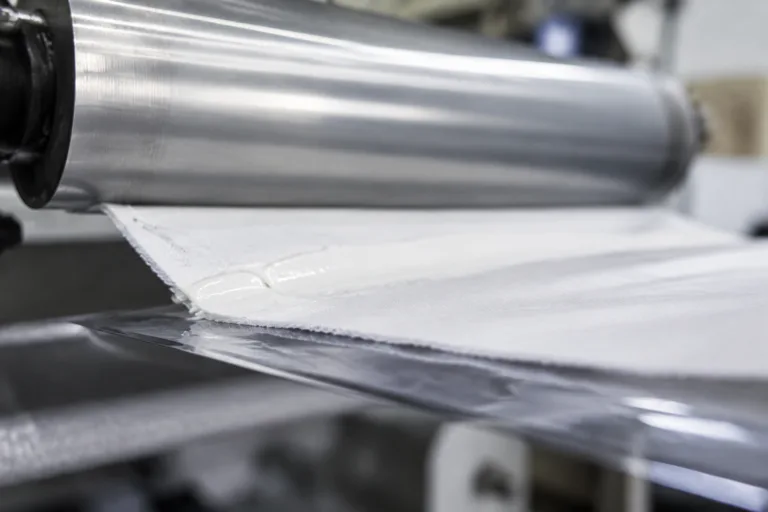 A realistic close-up product photo of adhesive bonding between fabric and film layers in a technical textile production setting.