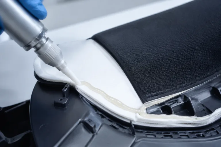 A realistic close-up product photo of fabric being bonded to a molded plastic component with adhesive in a clean mixed-material manufacturing setup.