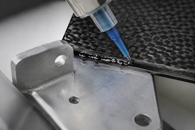 Metal Adhesive 6 A detailed close-up scene of metal-to-composite bonding adhesive being applied between a metal component and a composite or carbon fiber panel in a modern lightweight manufacturing environment.