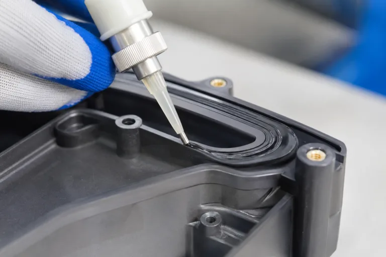 Plastic Adhesive 6 A realistic close-up product photo showing plastic-to-rubber bonding adhesive applied between a plastic housing and a rubber seal or gasket, with a visible flexible adhesive layer in a professional manufacturing setting.