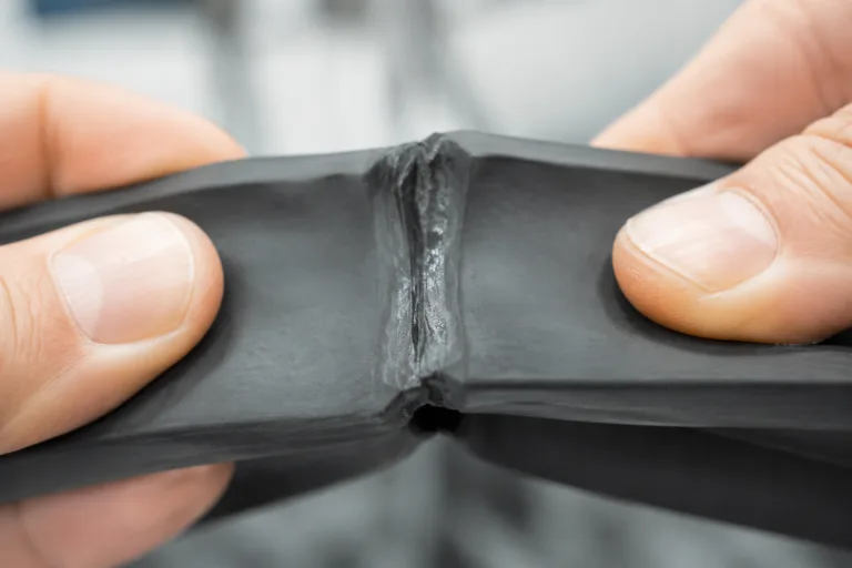 Rubber Adhesive 3 A realistic close-up product photo showing rubber-to-rubber bonding adhesive application with two flexible rubber pieces joined by a visible elastic seam in a clean industrial setting.