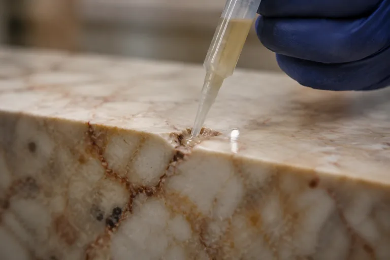 Stone Adhesive 6 A realistic close-up scene of a professional using resin or adhesive to carefully fill a chip or crack in a marble or granite surface during a stone restoration process.