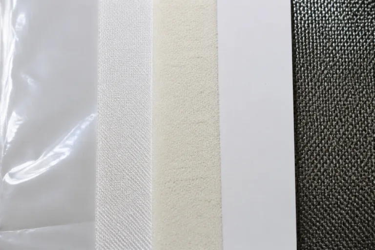 Laminating Adhesive 11 A realistic close-up product photography scene comparing several material surfaces used for adhesive lamination decisions, including smooth plastic film, porous fabric, soft foam, coated panel, and textured composite material, presented in a clean industrial style.